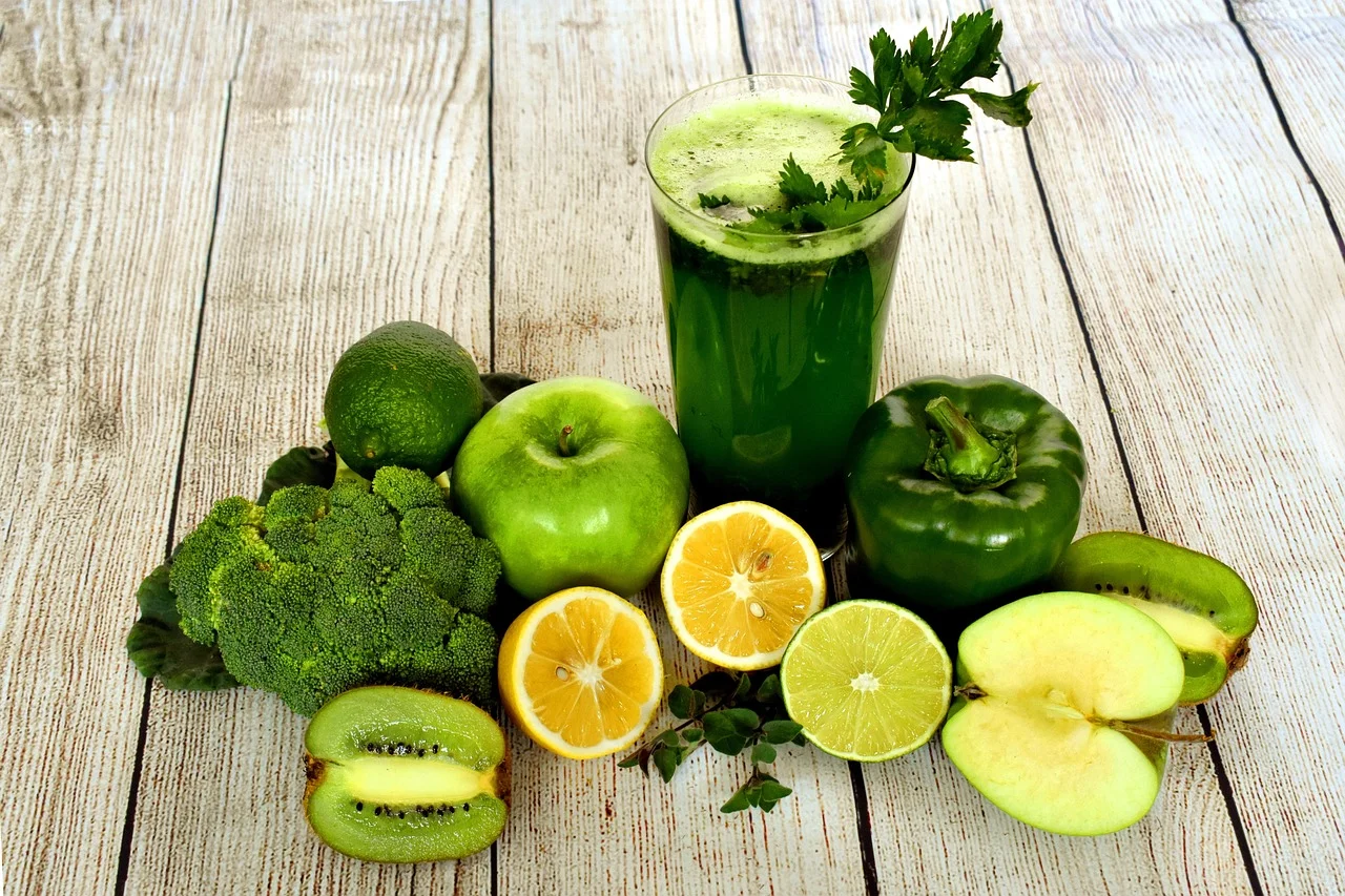 Glas groene smoothie op een houten tafel, met broccoli, appel, kiwi, limoen, citroen en paprika ernaast